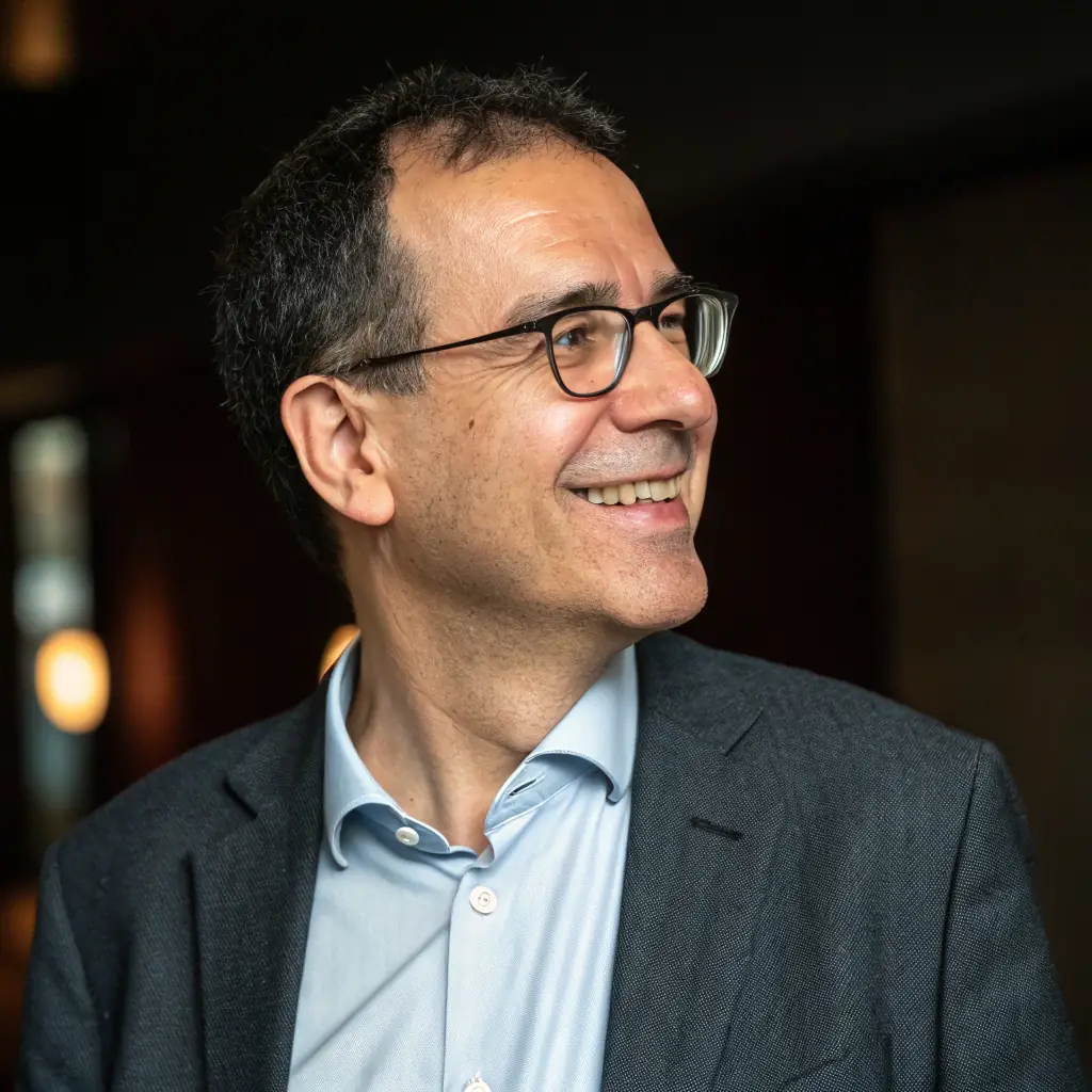 A professional portrait of a smiling middle-aged French man with short brown hair and glasses, wearing a suit and tie.